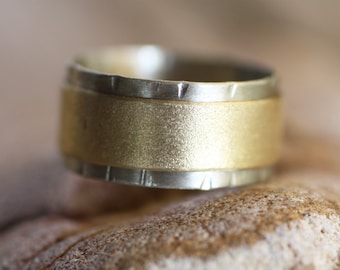 Puede incluir: Un anillo de oro y plata con una banda texturizada y un borde acanalado.