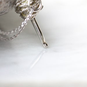 May include: A silver chain necklace with a small, silver, yarn ball charm. The charm has a silver needle attached to it.
