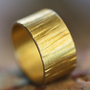 May include: A gold ring with a textured, brushed finish. The ring is wide and has a rounded shape.