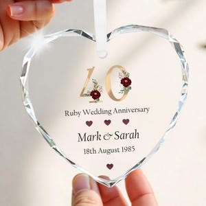 May include: A clear, heart-shaped crystal ornament with a white ribbon. The ornament features gold numerals "40" with floral accents, the text "Ruby Wedding Anniversary", names, and the date "18th August 1985".