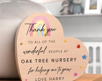 May include: Heart-shaped wooden plaque with a rainbow and the words "Thank you" and "Oak Tree Nursery." The plaque includes decorative bees, stars, and flowers. The message is "for helping me to grow, Love Harry."