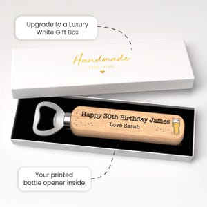 Puede incluir: Un abridor de botellas de madera con cabezal plateado, dentro de una caja de regalo blanca. El abridor est&aacute; grabado con "Happy 30th Birthday James Love Sarah" y una ilustraci&oacute;n de un vaso de cerveza. La caja est&aacute; etiquetada como "Handmade".