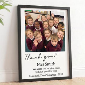 May include: A framed print featuring a group photograph of children in maroon jumpers, with the text "Thank you Mrs Smith We were the luckiest class to have you this year Love Oak Tree Class 2025 - 2026" printed in black on a white background.