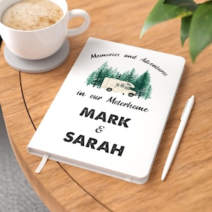 May include: White notebook with the text "Memories and Adventures in our Motorhome Mark & Sarah" and a cartoon illustration of a motorhome driving through a forest.