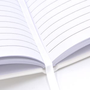 An open white notebook with lined pages, secured by a white ribbon.