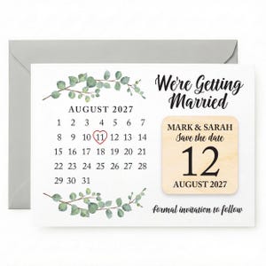 May include: A save-the-date card featuring a calendar highlighting August 11, 2027, with the text "We're Getting Married." A wooden accent displays "Mark & Sarah" and "August 12, 2027." Eucalyptus sprigs decorate the card.