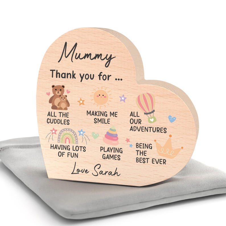 K&ouml;nnte beinhalten: Ein herzf&ouml;rmiges Holzschild mit dem Wort "Mummy" in Schreibschrift. Das Schild zeigt Illustrationen eines B&auml;ren, einer Sonne, eines Hei&szlig;luftballons, eines Regenbogens und einer Krone. Der Text enth&auml;lt "Thank you for..." und "Love Sarah."