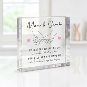 May include: A clear acrylic block with the words "Mum & Sarah" in script above a line drawing of two hands holding pinky fingers. The text "NO MATTER WHERE WE GO..." is below the hands, with two pink hearts.