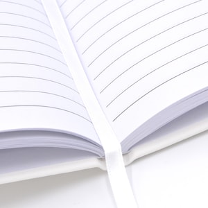 An open white notebook with lined pages, secured by a white ribbon.