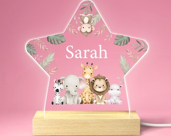 Può includere: Una luce notturna a forma di stella rosa con una base in legno. La stella presenta un tema di animali della giungla con una giraffa, un elefante, una zebra, un leone e una scimmia. Il nome "Sarah" è scritto in bianco sulla stella.