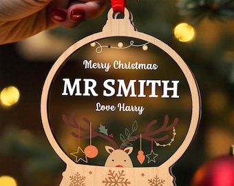 May include: A round wooden Christmas ornament with a clear center featuring the text Merry Christmas, MR SMITH, and Love Harry. The design includes a reindeer graphic with hanging star and bauble ornaments, plus snowflake engravings at the base.