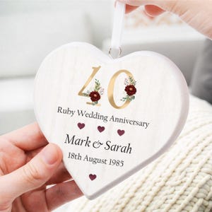 May include: A heart-shaped wooden plaque celebrating a Ruby Wedding Anniversary. The design includes the number 40 in gold, decorated with floral details. Text reads "Ruby Wedding Anniversary," names "Mark & Sarah," and the date "18th August 1985." A white ribbon is attached.