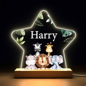 以下が含まれることがあります： 白い文字で「Harry」と書かれた星型のナイトライト。シマウマ、キリン、ライオン、カバ、ゾウのイラストが描かれたジャングルをテーマにしたライトです。緑の葉が星の縁を飾り、ベースは木製です。