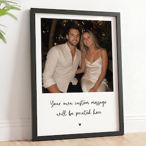 May include: A rectangular black picture frame containing a photograph of a couple sitting together. Below the photo, the white mat features the black printed text: Your own custom message will be printed here, followed by a small black heart icon.