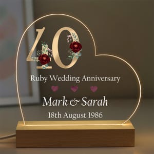 May include: A heart-shaped LED light, celebrating a 40th wedding anniversary. The text reads "Ruby Wedding Anniversary", with the names "Mark & Sarah" and the date "18th August 1986". The number 40 is adorned with floral details, and the base is wood.