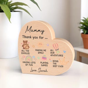 K&ouml;nnte beinhalten: Herzf&ouml;rmige Holzplakette mit den Worten "Mummy" und "Thank you for..." aufgedruckt. Die Plakette zeigt Illustrationen eines Teddyb&auml;ren, eines Regenbogens, eines Hei&szlig;luftballons und anderer Grafiken. Die Worte "Love Sarah" sind ebenfalls aufgedruckt.