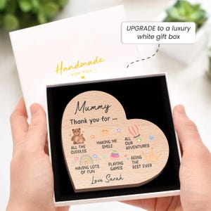 K&ouml;nnte beinhalten: Ein herzf&ouml;rmiges Holzschild mit der Aufschrift "Mummy, Thank you for..." und Illustrationen, pr&auml;sentiert in einer wei&szlig;en Geschenkbox. Das Schild enth&auml;lt S&auml;tze wie "All the cuddles" und "Love Sarah". Die Box ist mit "Handmade" beschriftet.