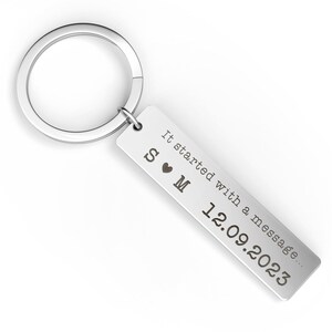 May include: A silver rectangular keychain with a circular ring. The keychain has the text "It started with a message..." and the date "12.09.2023" engraved on it. The initials "S &hearts; M" are also engraved on the keychain.