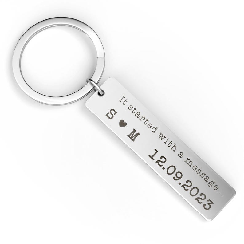 May include: A silver rectangular keychain with a circular ring. The keychain has the text "It started with a message..." and the date "12.09.2023" engraved on it. The initials "S &hearts; M" are also engraved on the keychain.