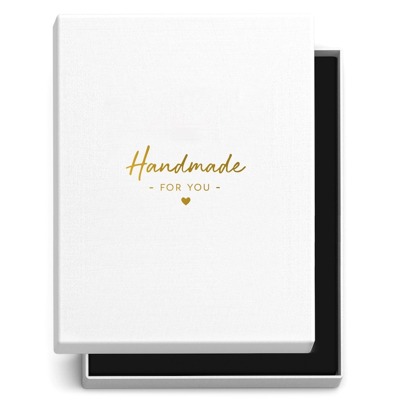 May include: A white rectangular gift box with the lid slightly open, revealing a black interior. The lid features the gold text "Handmade - FOR YOU -" with a small heart symbol. The box is designed for presenting gifts.