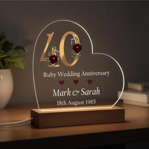 May include: A heart-shaped acrylic light-up sign with the number 40 in gold, red flowers, and the text "Ruby Wedding Anniversary", "Mark & Sarah", and "18th August 1985". The sign is on a wooden base.