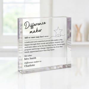 May include: A clear rectangular acrylic block featuring black printed text that defines the term Difference maker. The text includes a phonetic pronunciation, a dictionary-style definition, a star icon, and the names Mrs Smith and Charlotte.