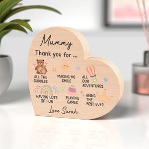 K&ouml;nnte beinhalten: Herzf&ouml;rmige Holzplakette mit der Aufschrift "Mummy Thank you for..." und verschiedenen Illustrationen. Der Text enth&auml;lt "All the cuddles", "Making me smile" und den Namen "Sarah".