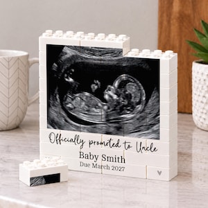 May include: A white building block display frame featuring a black and white ultrasound image. The text reads: Officially promoted to Uncle, Baby Smith, Due March 2027. A small matching block piece sits in front of the main rectangular frame structure.