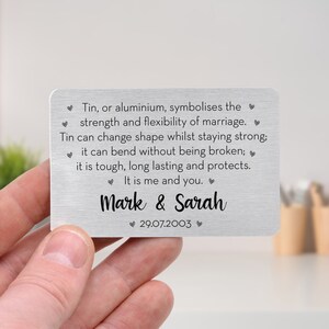May include: A rectangular, brushed metal card with rounded corners. The card features the names "Mark & Sarah" and the date "29.07.2003" in black script. Text about marriage strength and flexibility is also present.