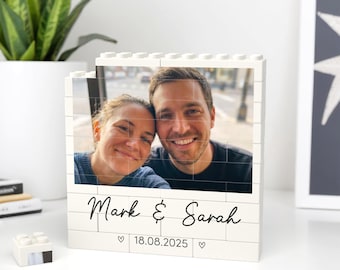 May include: A white brick-style photo frame featuring a smiling couple. The frame is personalized with the names "Mark & Sarah" and the date "18.08.2025" in black script. A small white Lego brick is in the foreground.