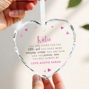 Puede incluir: Un adorno transparente en forma de coraz&oacute;n con un dise&ntilde;o facetado. El adorno tiene una cinta blanca para colgar y presenta el nombre "Katie" en escritura rosa, junto con un mensaje de amor y peque&ntilde;os corazones rosas.