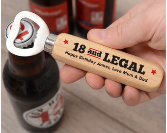 May include: A wooden bottle opener with the text "18 and LEGAL" and "Happy Birthday James, Love Mum & Dad" printed on it. The opener is silver and is removing the cap from a brown beer bottle.