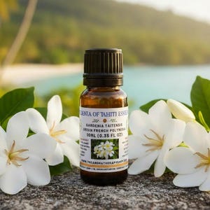 Könnte beinhalten: Eine braune Glasflasche mit ätherischem Öl und schwarzem Verschluss, beschriftet mit "Gardenia Taitensis" und "10ml (0,35 fl oz)". Die Flasche ist von weißen Gardenienblüten und grünen Blättern umgeben. Der Hintergrund zeigt eine Strandszene.