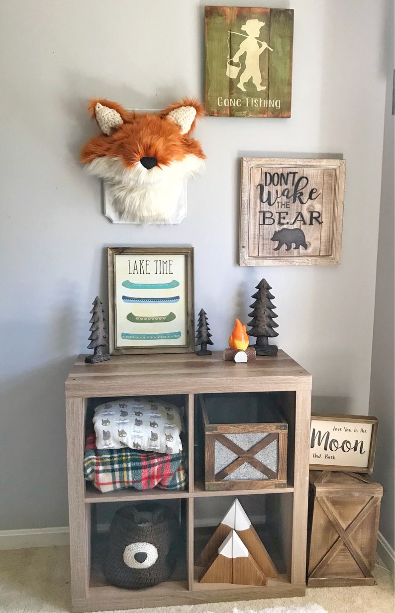 May include: A rustic-themed room decor arrangement featuring a faux fox head, wooden signs with text, and decorative items. The signs read "Gone Fishing", "Don't Wake the Bear", and "Lake Time". The arrangement includes a wooden cube shelf with blankets, a bear-shaped pillow, and wooden mountain blocks.