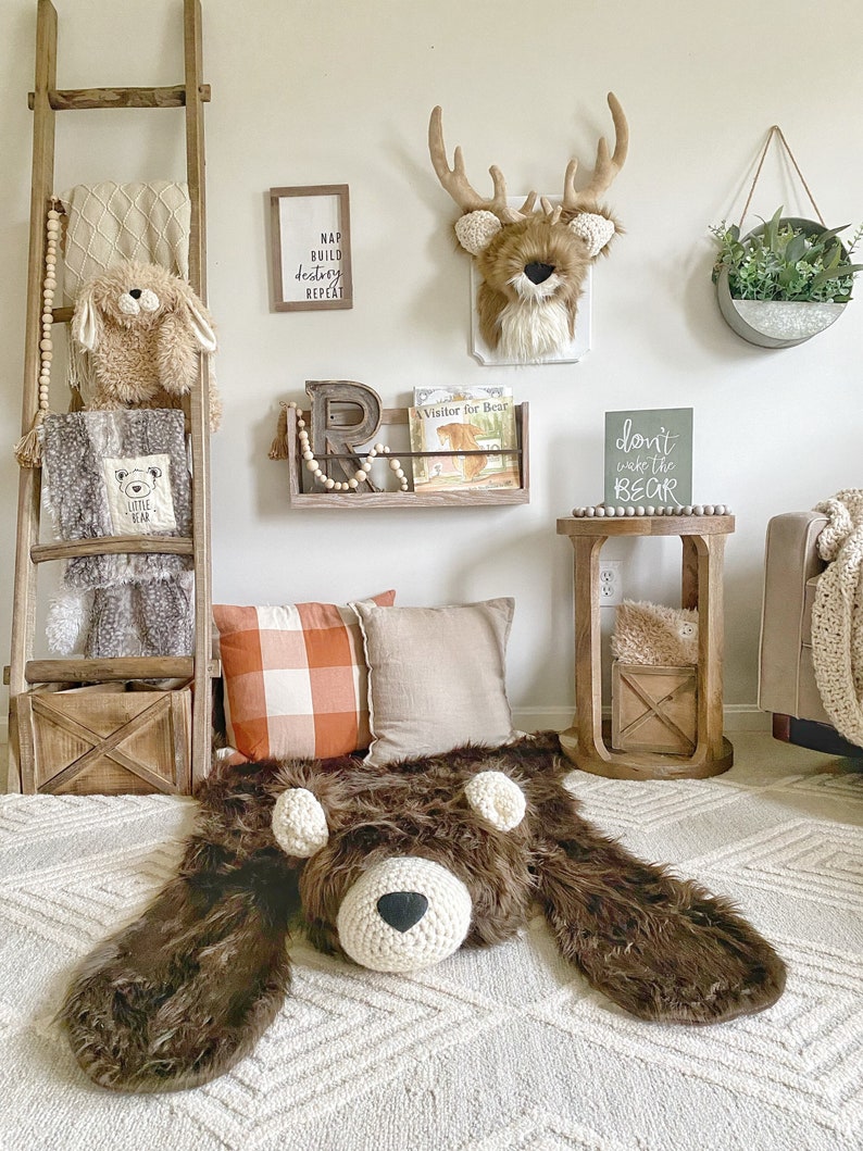 Plush Bear Rug on floor in kid room. With pillows and blanket ladder. Dont wake the bear sign hanging on the wall and wooden book shelf with books hanging under faux deer taxidermy