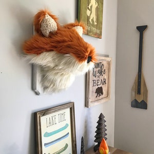 May include: A rustic wall display featuring a faux fox head, wooden signs with the phrases "Gone Fishing" and "Don't Wake the Bear", and a framed print that says "Lake Time". Decorative wooden canoe art and a campfire figurine are also present.