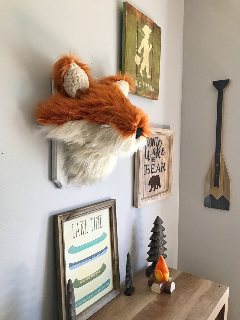 May include: A rustic wall display featuring a faux fox head, wooden signs with the phrases "Gone Fishing" and "Don't Wake the Bear", and a framed print that says "Lake Time". Decorative wooden canoe art and a campfire figurine are also present.