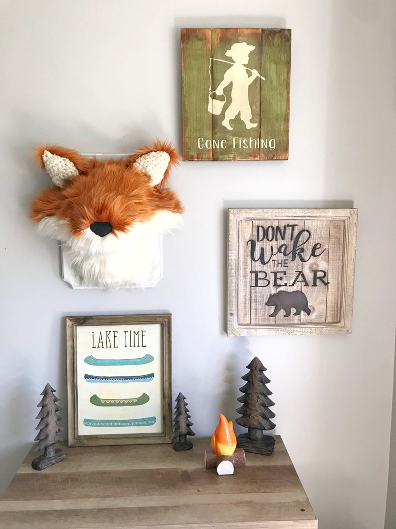 May include: A rustic wall decor arrangement featuring a faux fox head, framed signs, and wooden accents. The signs read "Gone Fishing" and "Don't Wake the Bear." A framed print displays canoes with the text "Lake Time."
