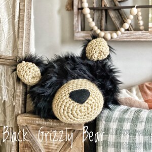 May include: A crocheted black grizzly bear head with a tan crocheted face and black felt nose. The bear head is sitting on a wooden box with the text "Black Grizzly Bear" written on the front.