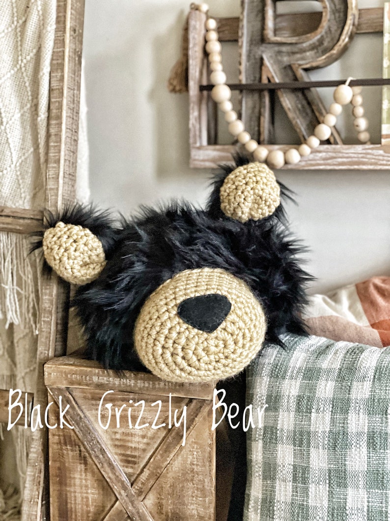 May include: A crocheted black grizzly bear head with a tan crocheted face and black felt nose. The bear head is sitting on a wooden box with the text "Black Grizzly Bear" written on the front.