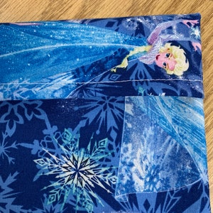 Op de afbeelding: Blauwe stoffen tas met een wit sneeuwvlokkenpatroon en een afbeelding van Elsa uit Frozen. De tas heeft een witte naad rond de bovenkant.