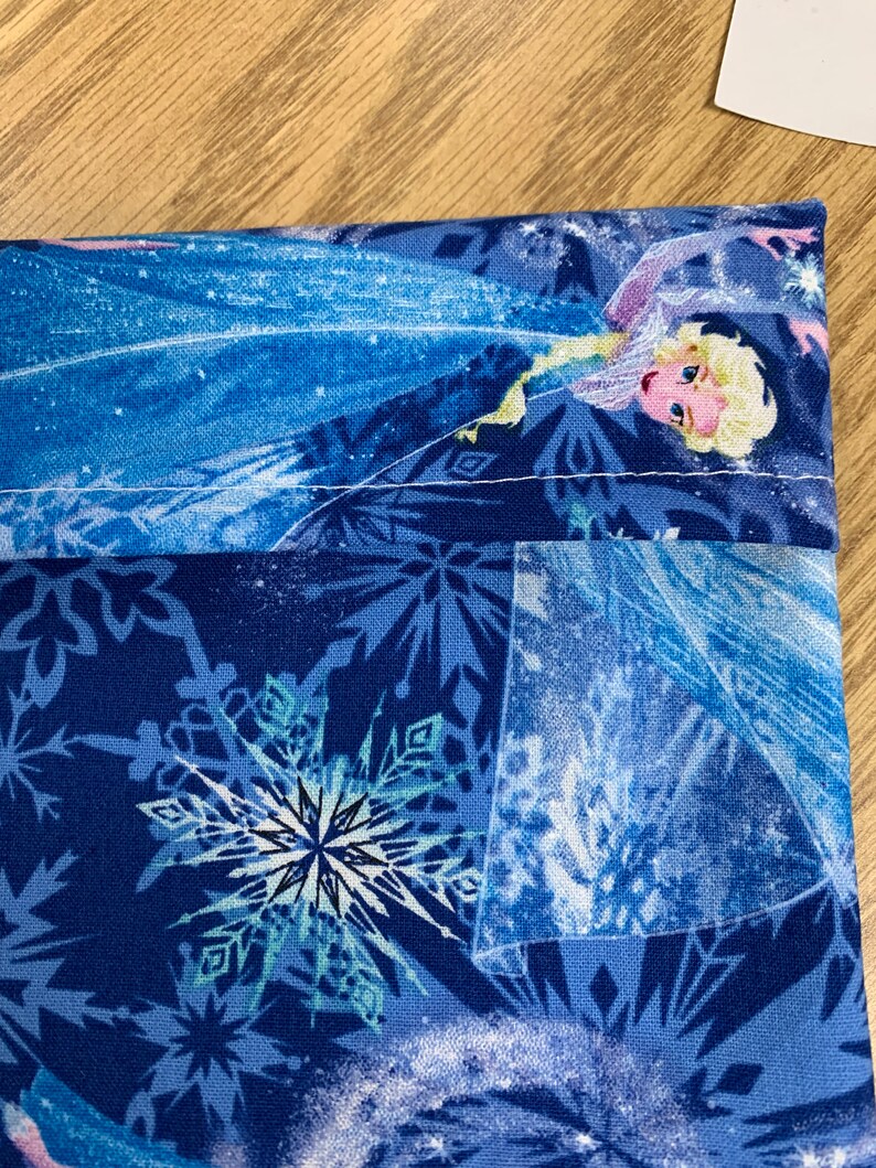 Op de afbeelding: Blauwe stoffen tas met een wit sneeuwvlokkenpatroon en een afbeelding van Elsa uit Frozen. De tas heeft een witte naad rond de bovenkant.
