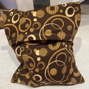 Op de afbeelding: Een bruine stoffen tas met een ritssluiting. De tas heeft een patroon van tan en witte cirkels en strepen.