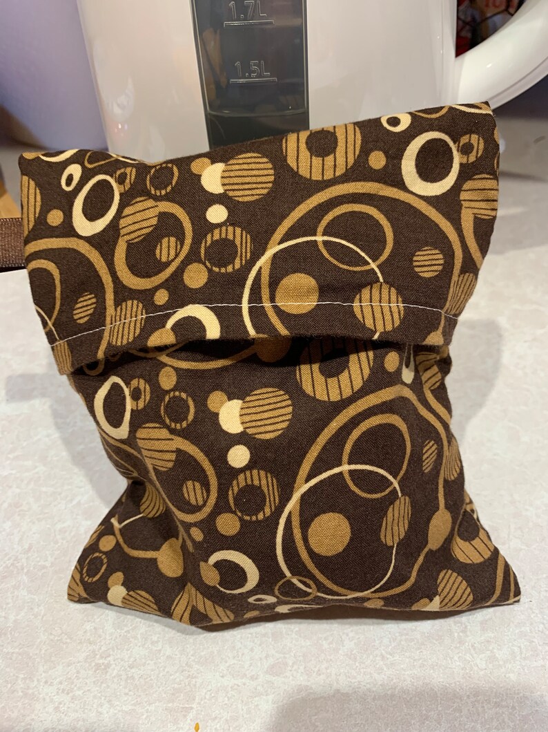 Op de afbeelding: Een bruine stoffen tas met een ritssluiting. De tas heeft een patroon van tan en witte cirkels en strepen.