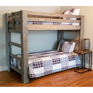 May include: A wooden bunk bed with a gray stain finish. The bottom bunk has a blue and white patterned quilt. A small black side table with a lamp sits next to the bed.