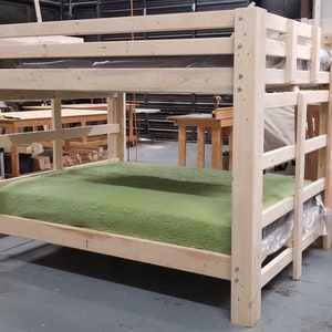 May include: A wooden bunk bed with a green mattress on the bottom bunk. The bed is made of unfinished wood and has a simple design.