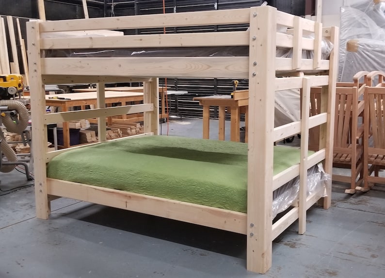 May include: A wooden bunk bed with a green mattress on the bottom bunk. The bed is made of unfinished wood and has a simple design.