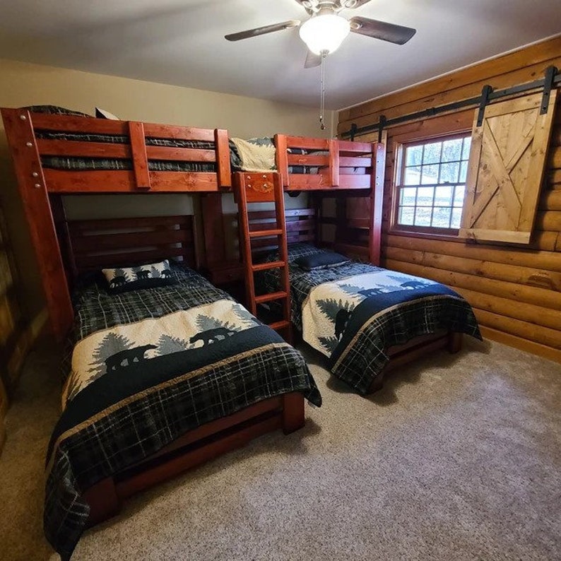 May include: A wooden bunk bed with a ladder and two mattresses. The mattresses are covered in black and white bedding with a bear print. The room has a wood-panelled wall with a window and a sliding barn door.