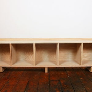 May include: A wooden shelf unit with five open compartments. The shelf is made of light wood and has a simple, modern design.