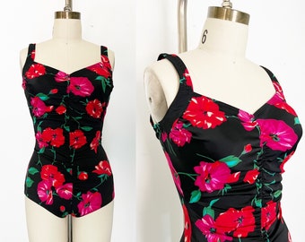 May include: A black one-piece swimsuit with a floral print featuring red and pink flowers on a black background. The swimsuit has a gathered detail at the bust and adjustable straps.